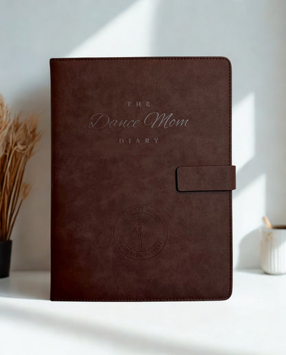 Brown leather Dance Mom Diary with embossed cover and strap closure with a white background and natural lighting.